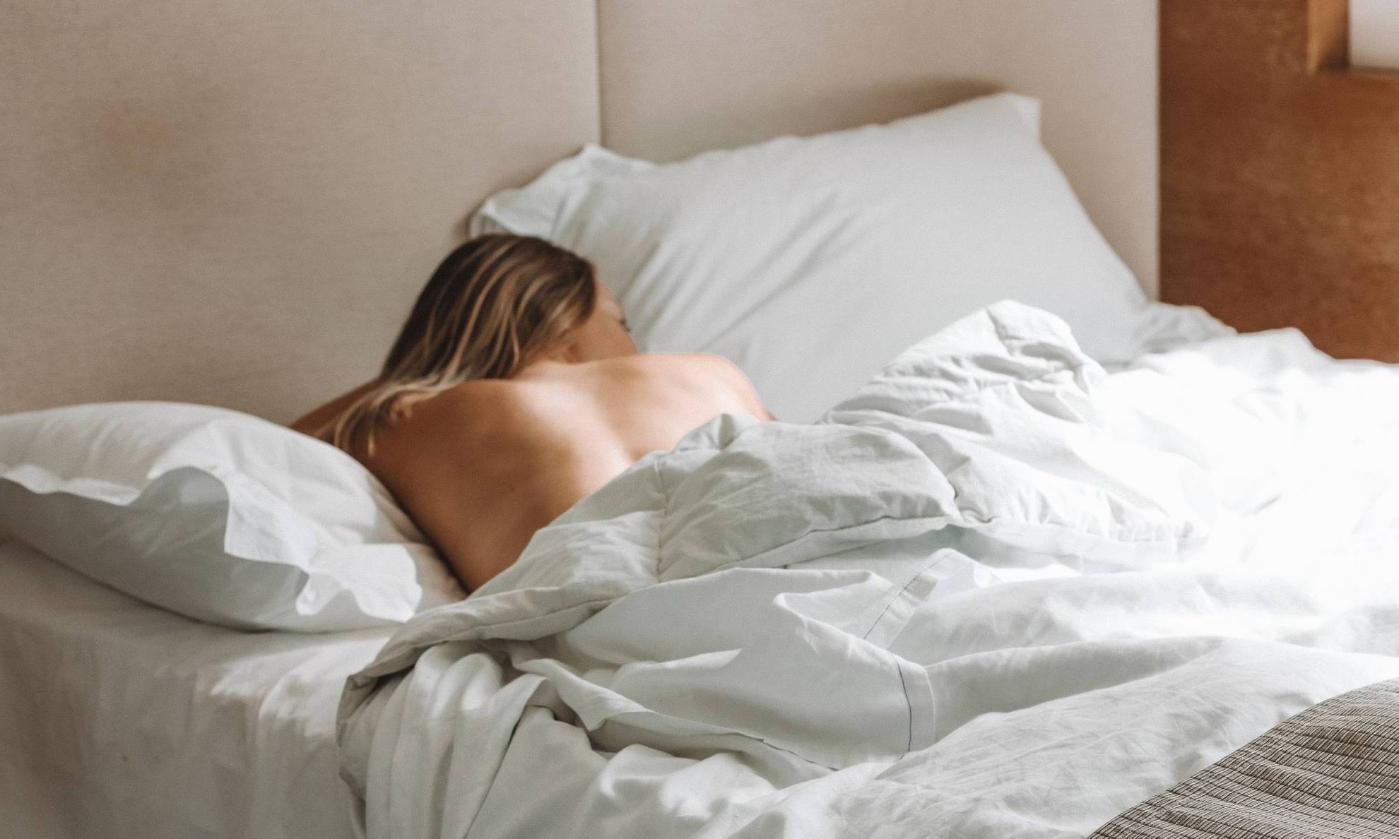 Девушка спит в постели, видно обнаженную спину
