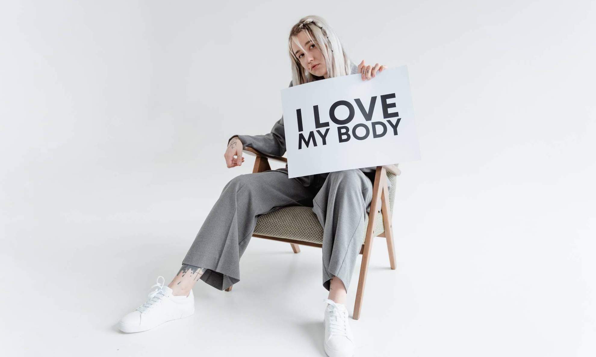 Девушка сидит на стуле с плакатом «Я люблю свое тело»
