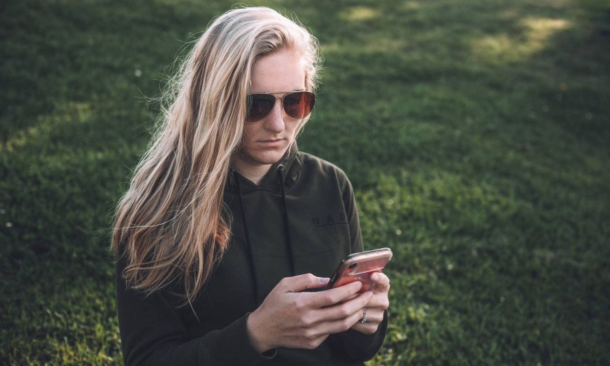 Девушка в солнечных очках с серьезным видом изучает смартфон